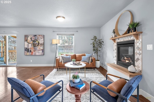 living area with a fireplace, a textured ceiling, baseboards, and wood finished floors