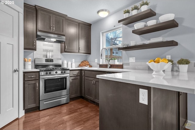 kitchen featuring dark brown cabinetry, under cabinet range hood, stainless steel gas range, open shelves, and dark wood finished floors