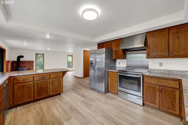915 Marquet Way, Eugene, OR 97401 - kitchen with wall chimney exhaust hood, appliances with stainless steel finishes, a wood stove, light wood-type flooring, and brown cabinets