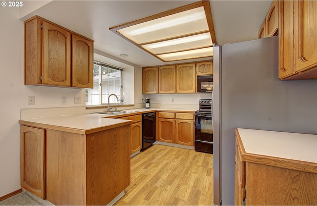 kitchen with light wood finished floors, brown cabinets, a peninsula, black appliances, and a sink