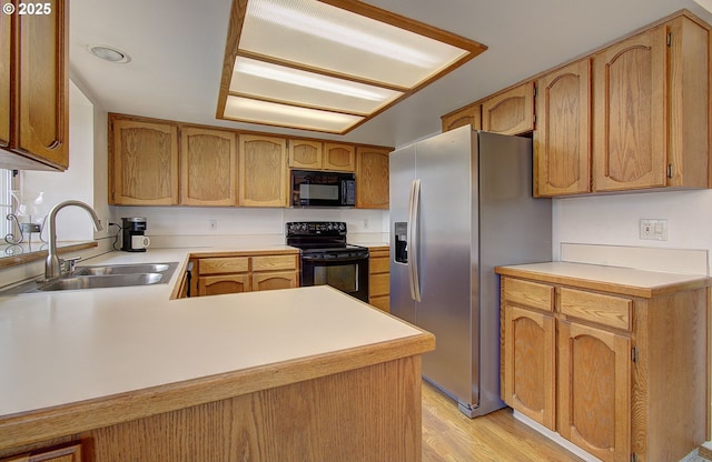 kitchen with light countertops, a peninsula, light wood-style floors, black appliances, and a sink