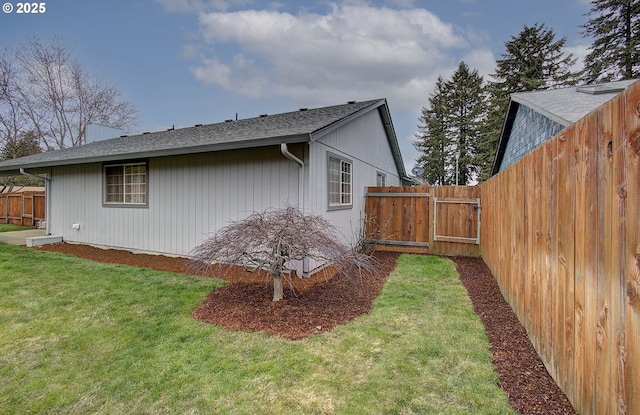 view of side of property with a lawn, a shingled roof, and fence