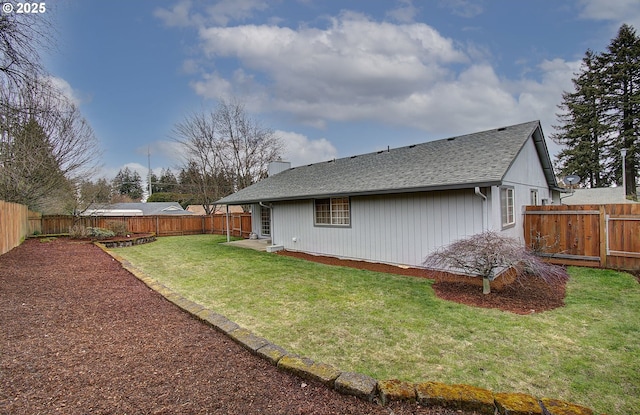 back of house with a fenced backyard, a chimney, a yard, and roof with shingles