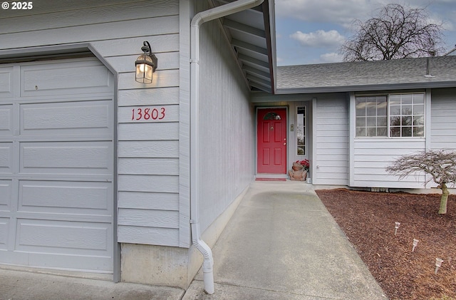 doorway to property with a garage and a shingled roof