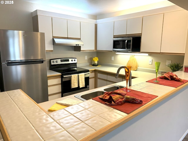 kitchen with stainless steel appliances, tile counters, a sink, and under cabinet range hood