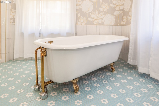 bathroom featuring a wainscoted wall, a soaking tub, and wallpapered walls