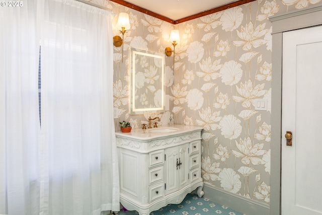 bathroom with wallpapered walls, vanity, crown molding, and baseboards