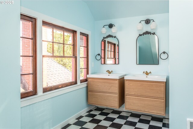 bathroom featuring tile patterned floors, vaulted ceiling, plenty of natural light, two vanities, and baseboards