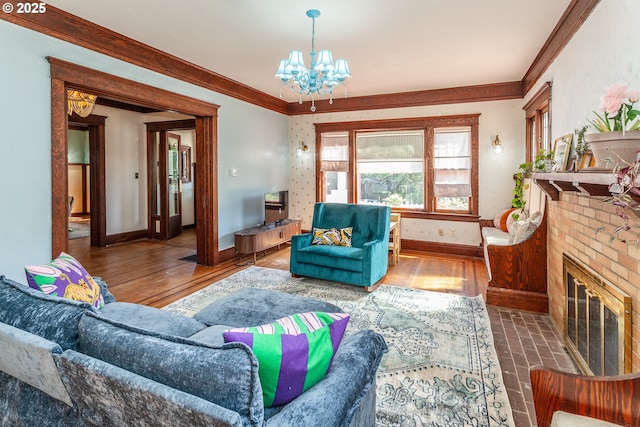 living room featuring a chandelier, baseboards, wood finished floors, ornamental molding, and a fireplace