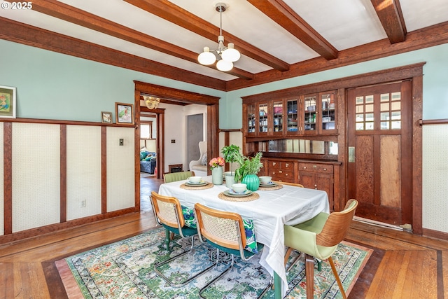 dining room with a chandelier, beam ceiling, hardwood / wood-style flooring, and baseboards