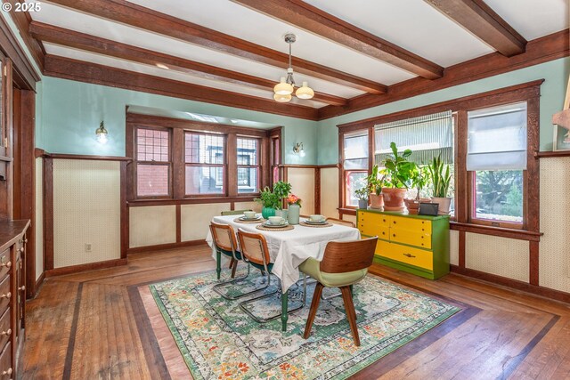 dining space with beamed ceiling, a chandelier, hardwood / wood-style flooring, and baseboards
