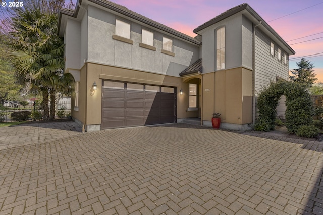 view of front of house with decorative driveway, a garage, and stucco siding