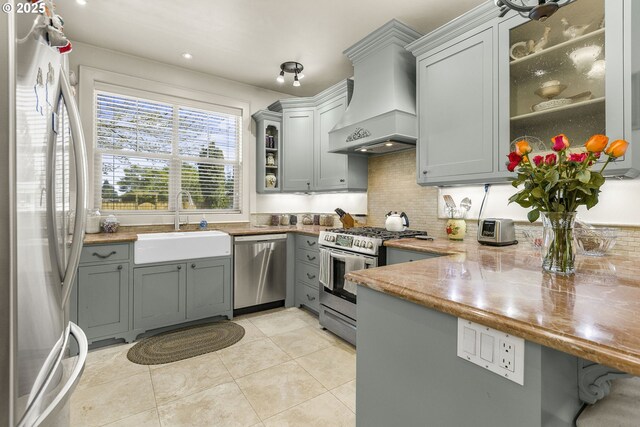 kitchen with appliances with stainless steel finishes, custom exhaust hood, a sink, gray cabinets, and a peninsula