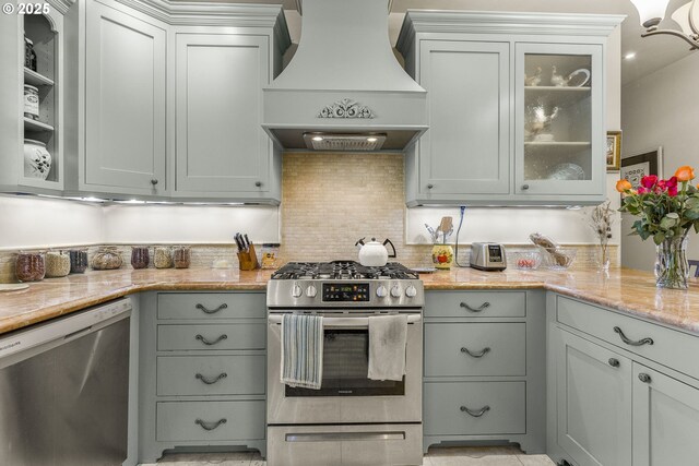kitchen with premium range hood, stainless steel appliances, tasteful backsplash, light stone countertops, and glass insert cabinets