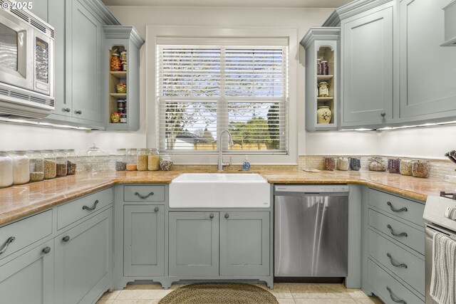 kitchen featuring stainless steel appliances, a sink, glass insert cabinets, open shelves, and light stone countertops