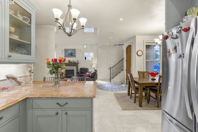 kitchen featuring freestanding refrigerator, a peninsula, a chandelier, glass insert cabinets, and decorative light fixtures
