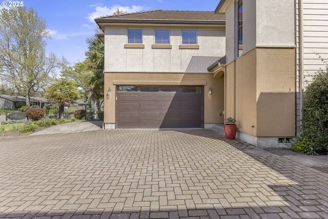 view of front of house with decorative driveway, a garage, fence, and stucco siding