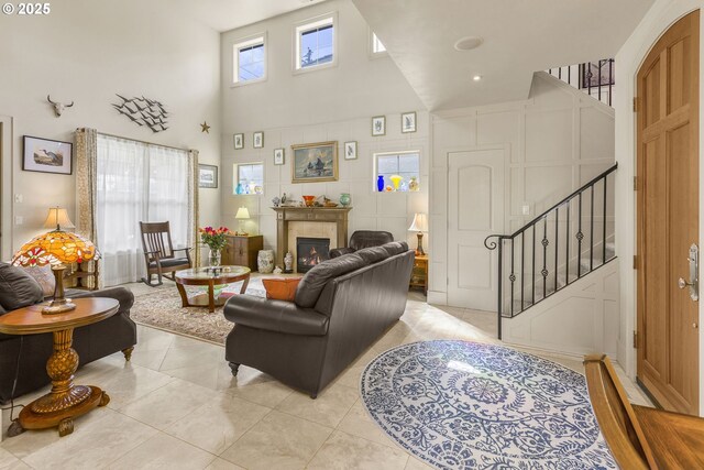 living room featuring a towering ceiling, stairway, a tile fireplace, and light tile patterned flooring