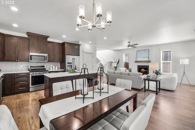 2522 S Lydia Loop, Hubbard, OR 97032 - dining area featuring a warm lit fireplace, a ceiling fan, recessed lighting, light wood finished floors, and a chandelier
