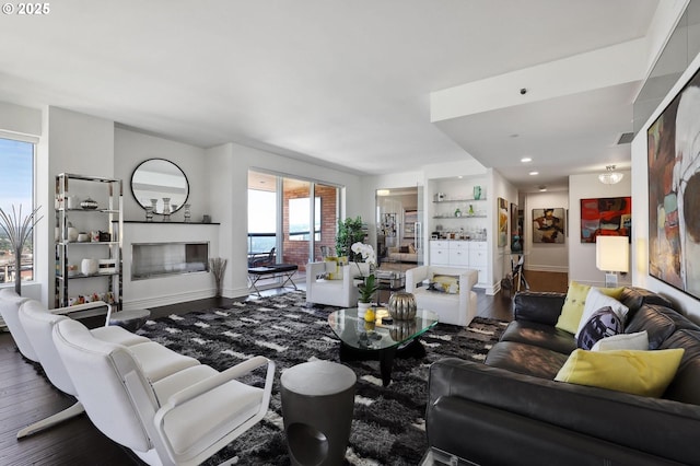 living room with wood finished floors, a glass covered fireplace, baseboards, and recessed lighting