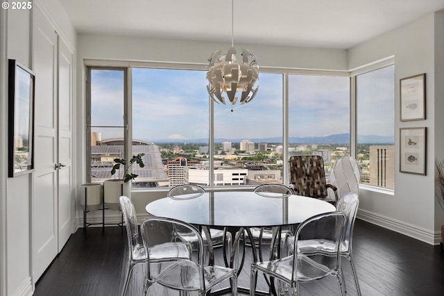 dining room with a chandelier, baseboards, dark wood-style floors, and a city view