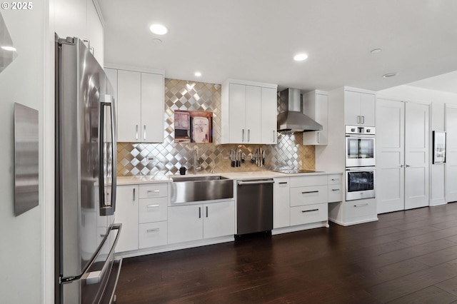 kitchen featuring wall chimney range hood, stainless steel appliances, a sink, light countertops, and decorative backsplash