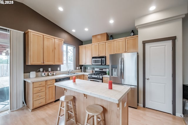 kitchen with a sink, light brown cabinetry, light wood-style flooring, and appliances with stainless steel finishes