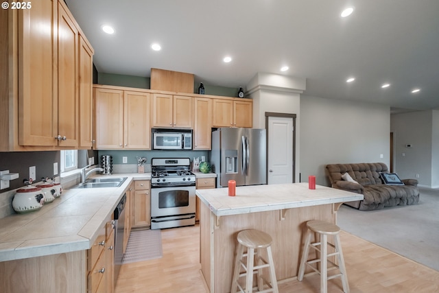 kitchen featuring a kitchen island, light brown cabinets, open floor plan, a sink, and appliances with stainless steel finishes