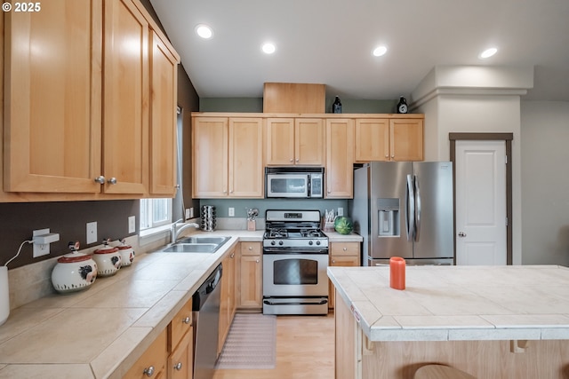 kitchen featuring light brown cabinetry, appliances with stainless steel finishes, a sink, light wood-style floors, and tile counters
