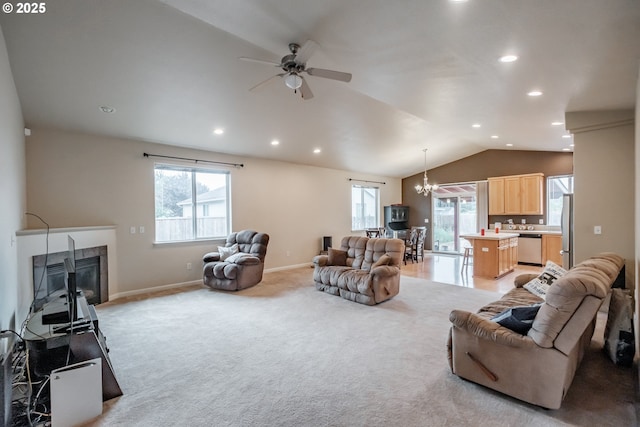 living room featuring vaulted ceiling, a healthy amount of sunlight, ceiling fan with notable chandelier, and a tile fireplace