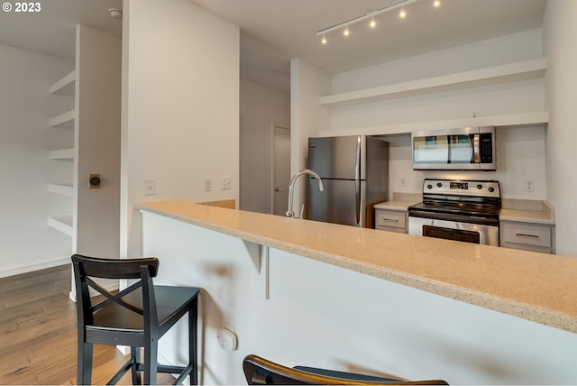 kitchen with light stone countertops, appliances with stainless steel finishes, a kitchen breakfast bar, and wood finished floors