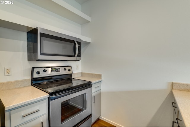 kitchen featuring appliances with stainless steel finishes, white cabinetry, and baseboards