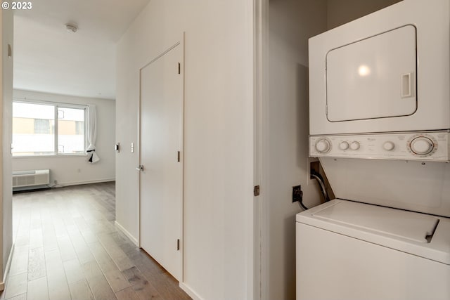 laundry area featuring stacked washer / drying machine, a wall mounted AC, wood finished floors, laundry area, and baseboards