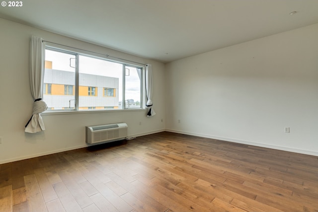 unfurnished room with a wall mounted air conditioner, wood finished floors, and baseboards