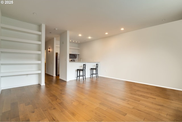 unfurnished living room with baseboards, wood finished floors, built in features, and recessed lighting