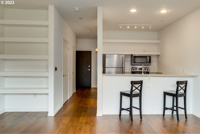 kitchen with stainless steel appliances, built in shelves, dark wood-style flooring, and a breakfast bar area