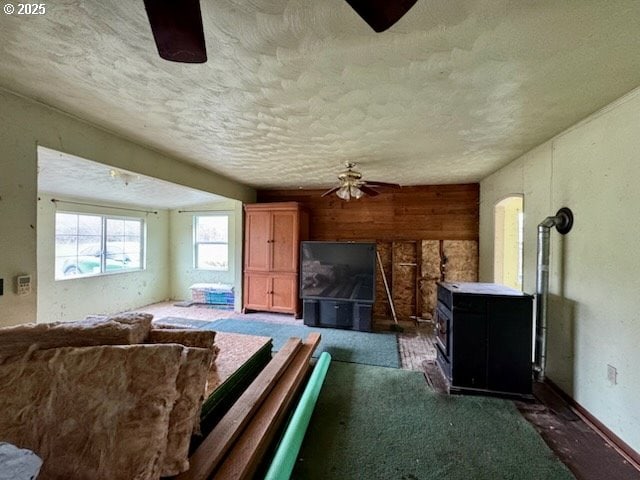 living room with dark colored carpet, a wood stove, ceiling fan, and wooden walls