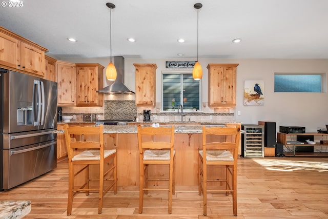 kitchen with beverage cooler, a kitchen breakfast bar, stainless steel refrigerator with ice dispenser, light stone countertops, and wall chimney range hood