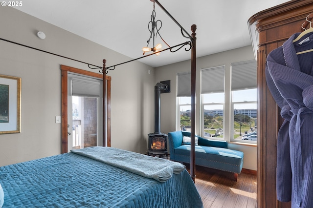 bedroom featuring multiple windows, wood finished floors, a wood stove, and a chandelier