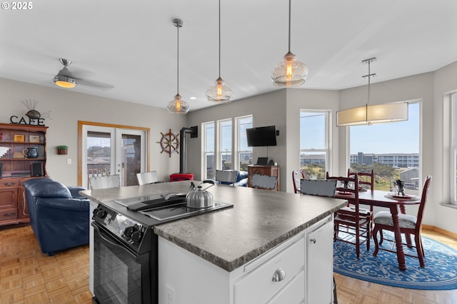 kitchen with black range with electric cooktop, open floor plan, dark countertops, white cabinets, and hanging light fixtures