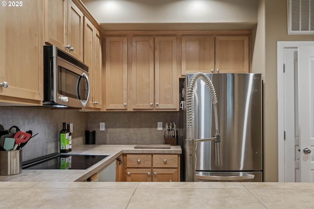 kitchen featuring tile countertops, stainless steel appliances, backsplash, and visible vents