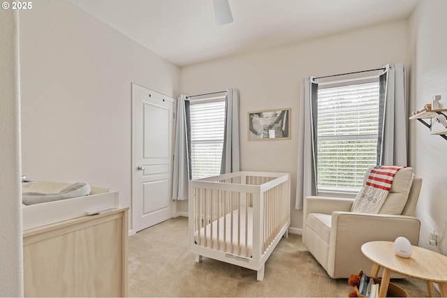 bedroom with a nursery area, baseboards, a ceiling fan, and light colored carpet