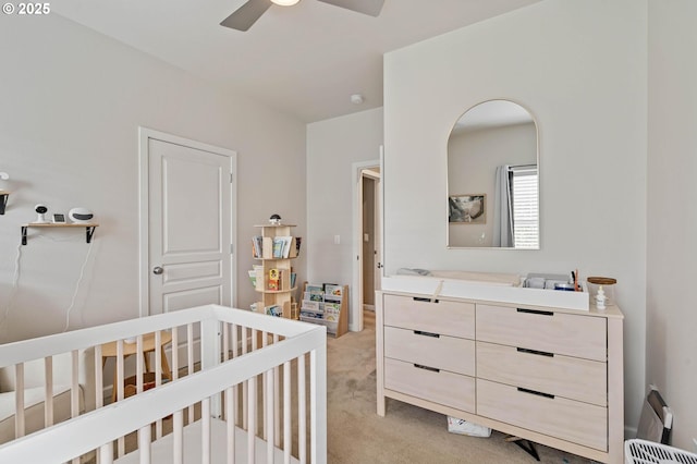 bedroom featuring a nursery area, light carpet, and ceiling fan