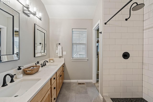 full bath featuring a sink, a tile shower, baseboards, and double vanity