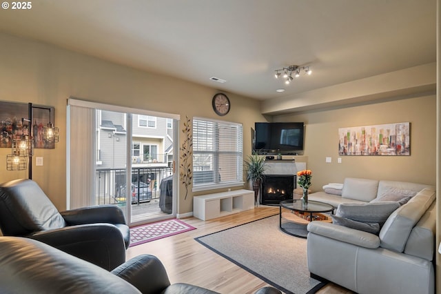 living room featuring visible vents, a lit fireplace, and wood finished floors