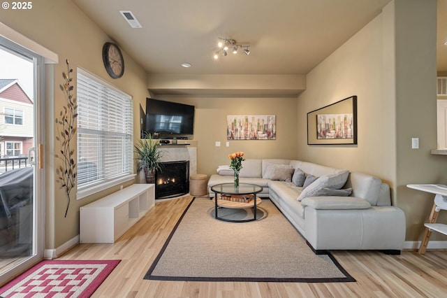 living area with light wood-style floors, visible vents, a fireplace, and baseboards