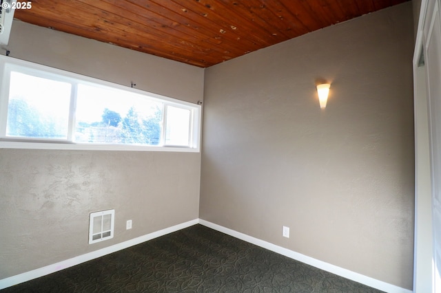 empty room featuring wood ceiling and dark colored carpet