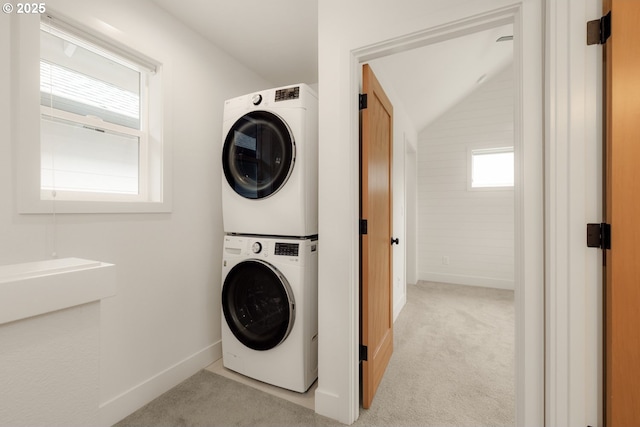 clothes washing area featuring light carpet, stacked washer and dryer, laundry area, and baseboards