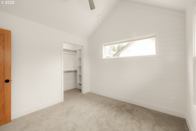 unfurnished bedroom with light colored carpet, a ceiling fan, vaulted ceiling, a spacious closet, and a closet