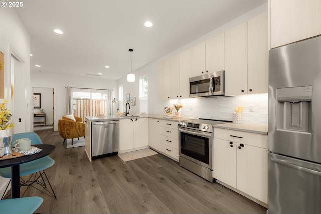 kitchen with stainless steel appliances, a sink, light countertops, decorative backsplash, and dark wood-style floors